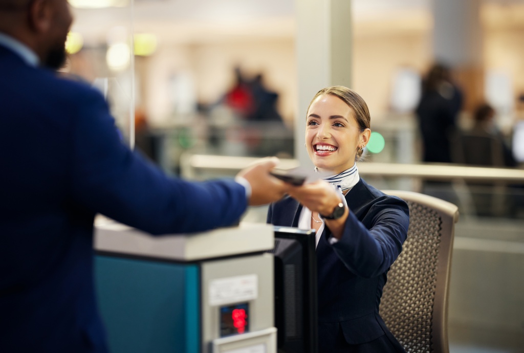 a smiling airline agent handing a customer their ticket